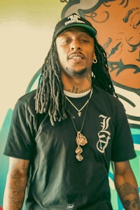 a man with dreadlocks standing in front of a colorful wall